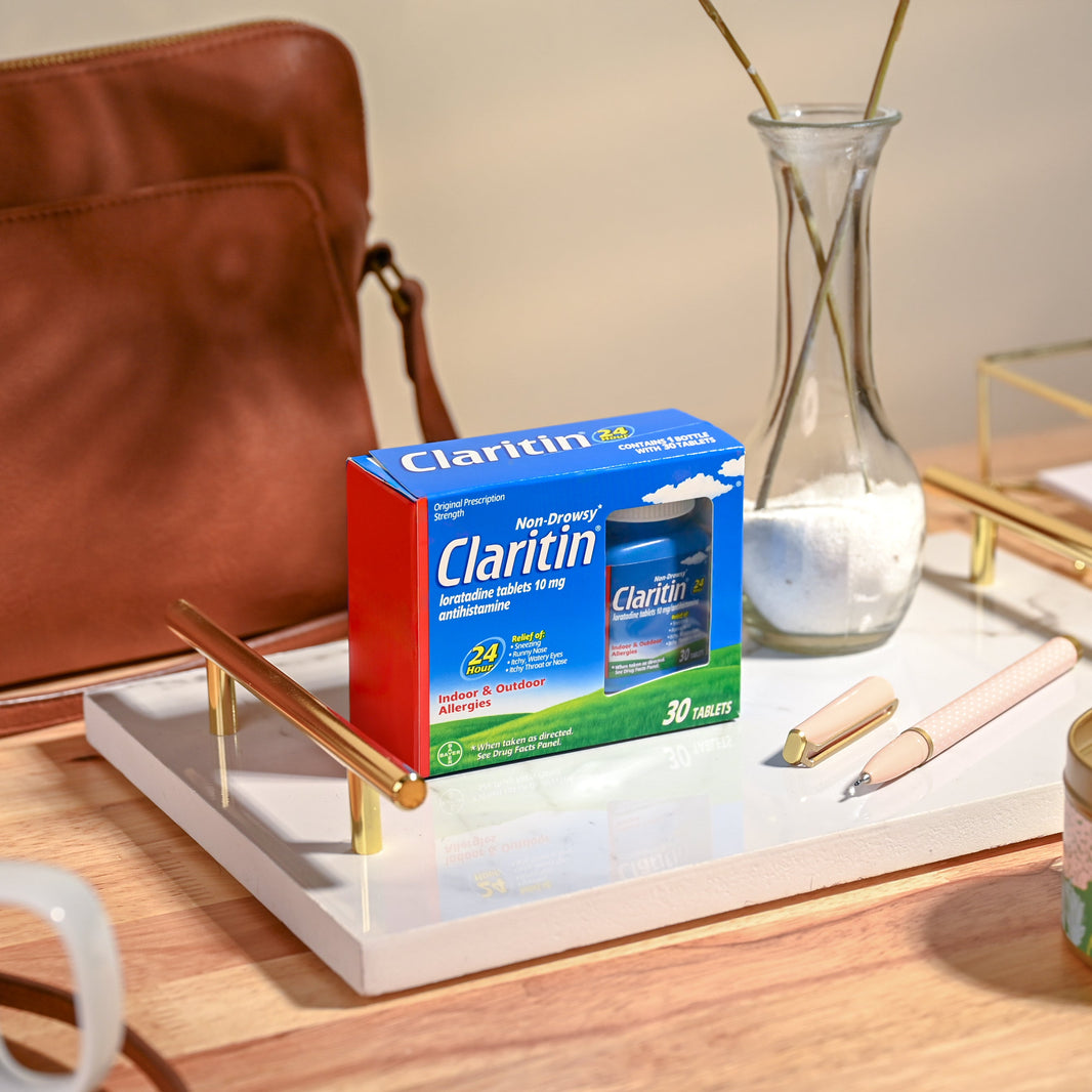 Claritin allergy medication box on a tray with a candle and coffee cup in the background