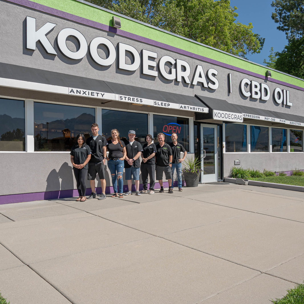Group of people standing outside a Koodegras CBD Oil store with mountains in the background.