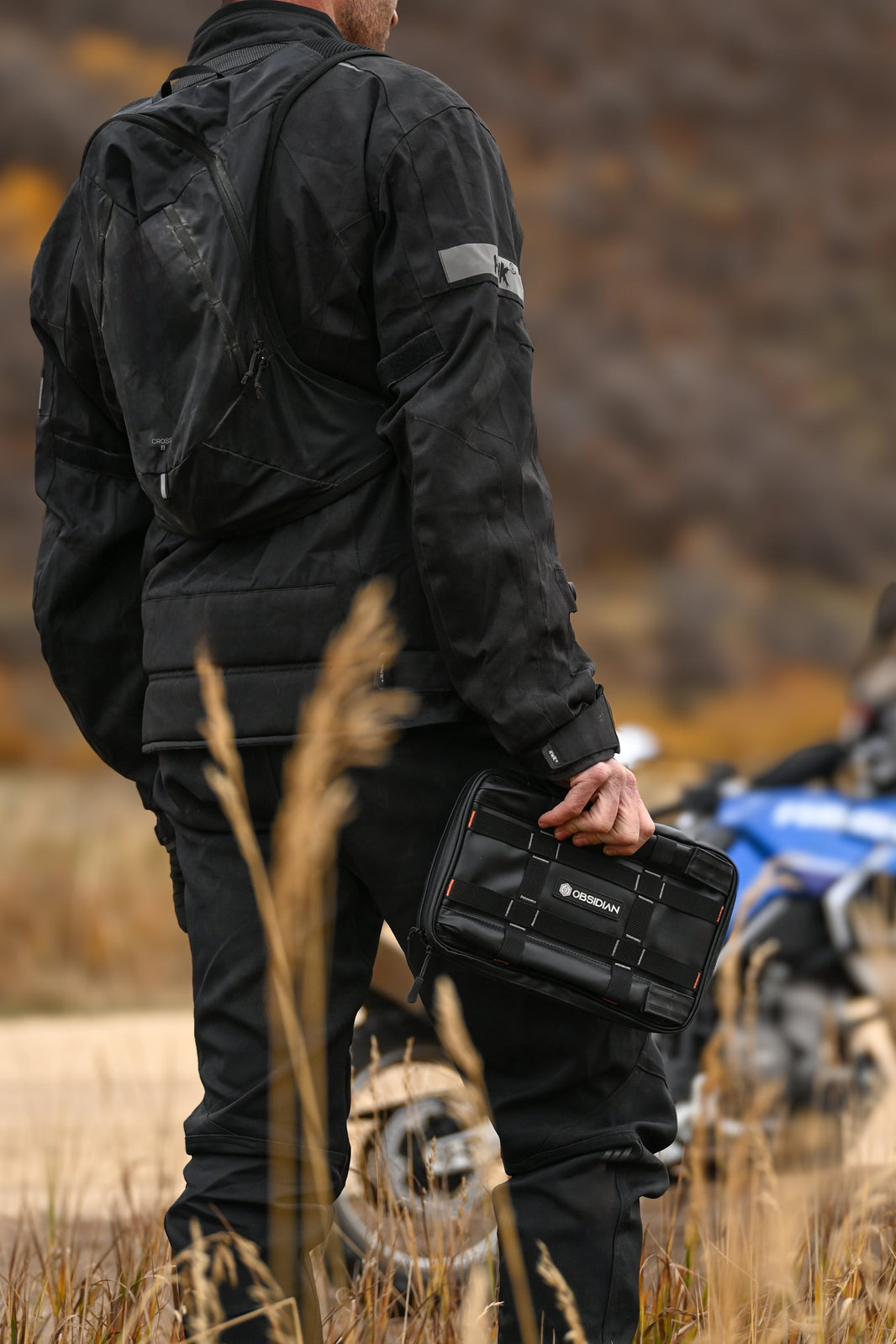 Person in black jacket holding a black case with motorcycles in the background
